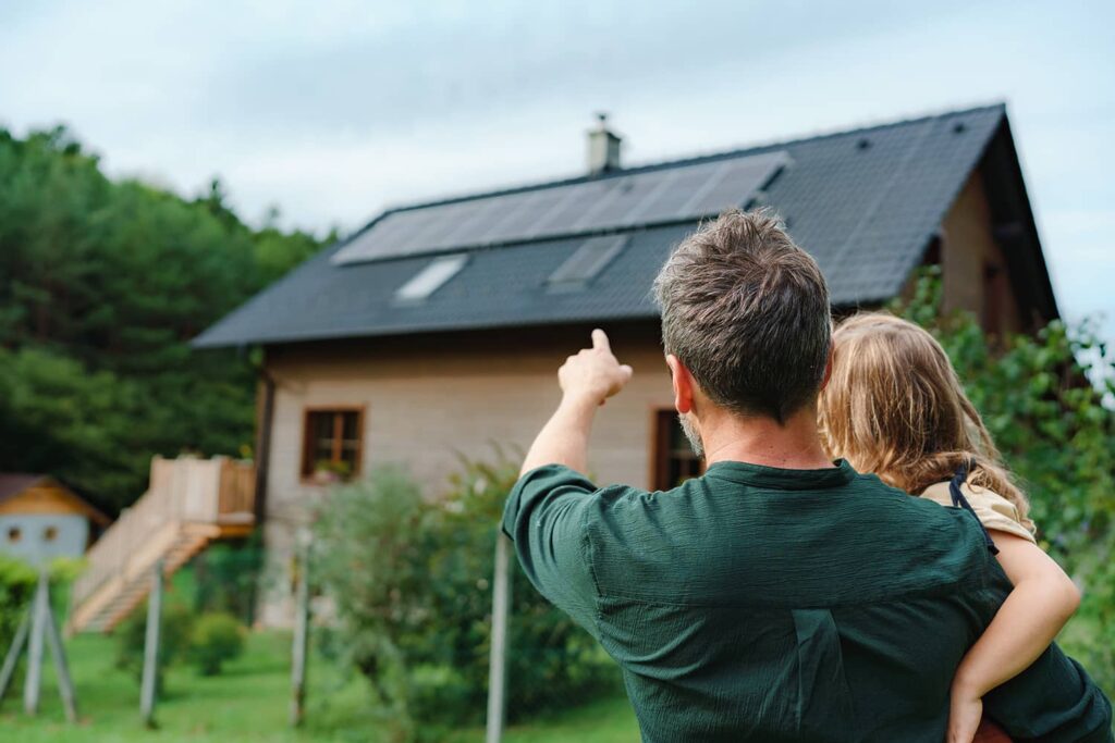 Un père et son enfant regardant une maison équipée de panneaux solaires
