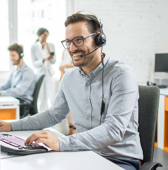 Photo d’un conseiller clientèle souriant, portant un casque et travaillant sur un ordinateur, illustrant le service client de Mega